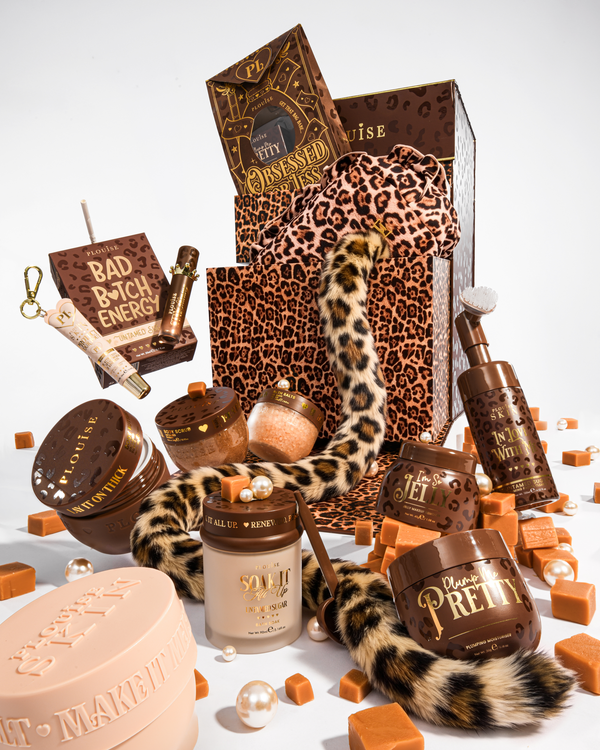 A luxury beauty gift set styled with brown and leopard print elements, including a leopard print gift bag, a leopard print tail, and multiple cosmetic containers in brown and beige tones, arranged on a white background with caramel-coloured cubes and pearls.