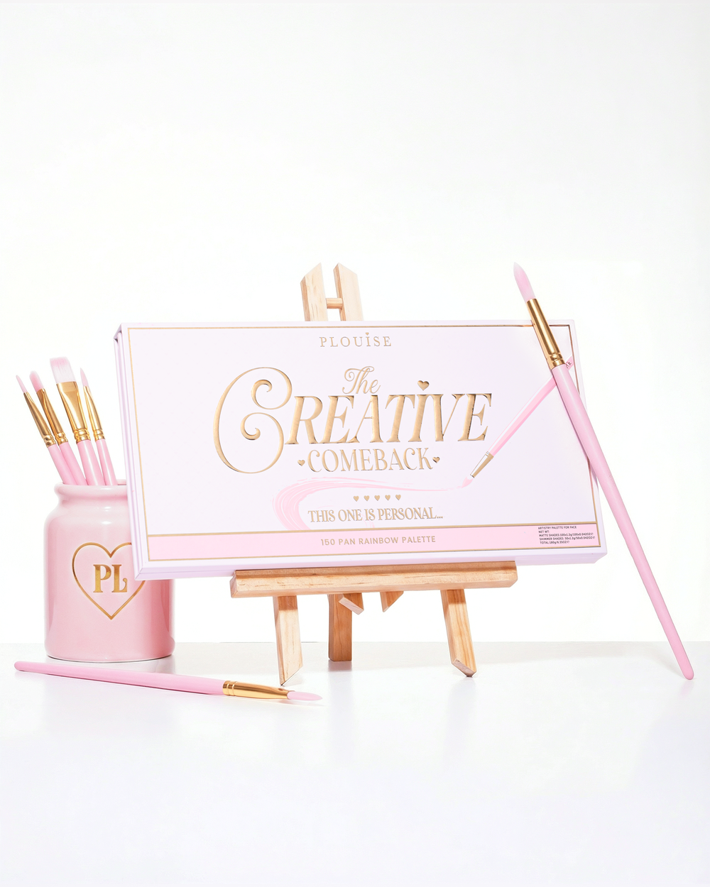 Zamknięta różowa paleta cieni do powiek P.Louise Creative Comeback XXXL Rainbow umieszczona na sztaludze artystycznej otoczonej pędzlami do makijażu