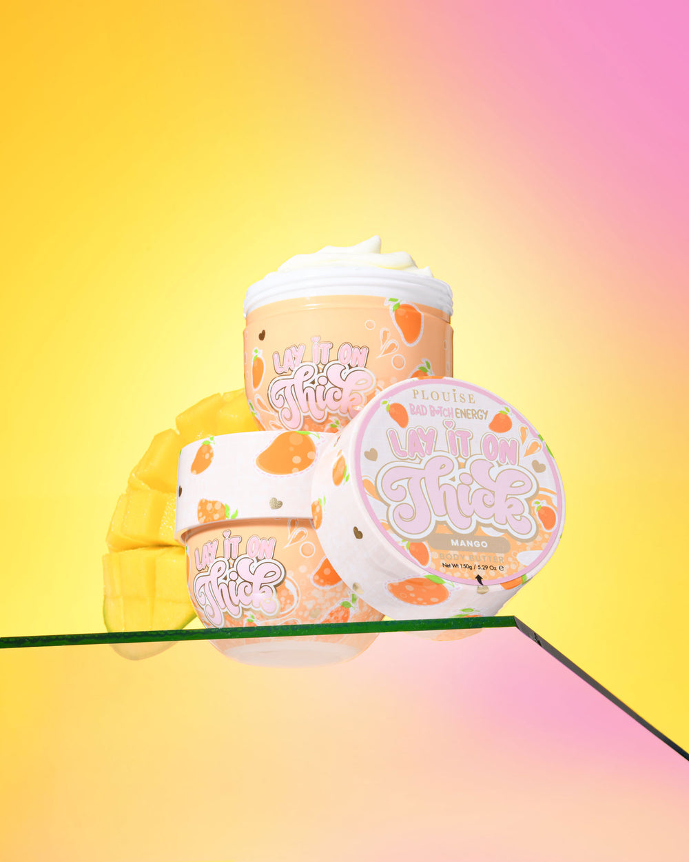 Trzy opakowania masła do ciała z mango P. Louise „Lift It On Thick” na gradientowym żółto-różowym tle