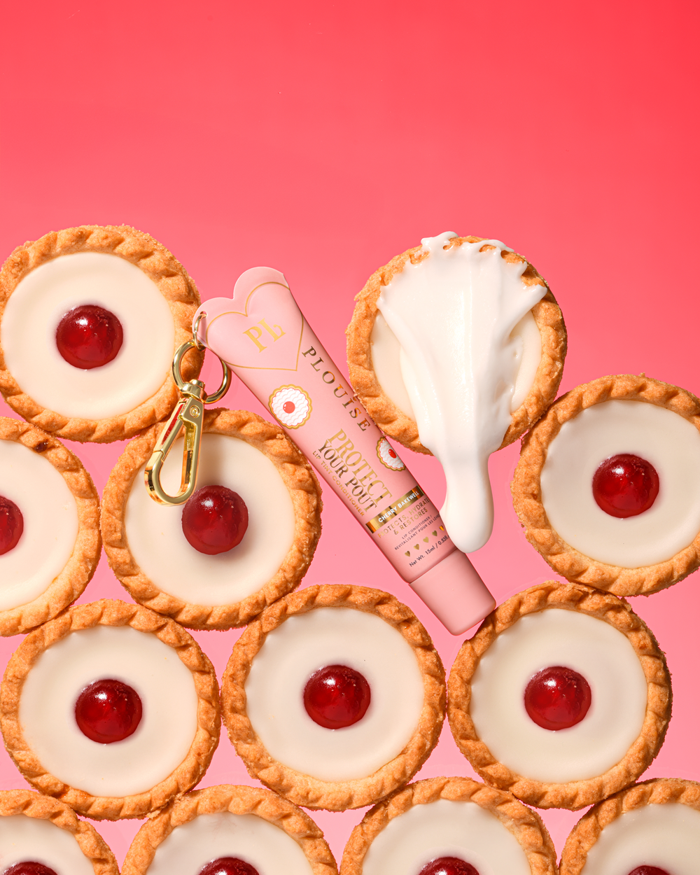 Barwiona różowo-wiśniowo-migdałowa odżywka do ust za pomocą złotego klipsa umieszczonego pomiędzy wiśniowymi deserami bakewell