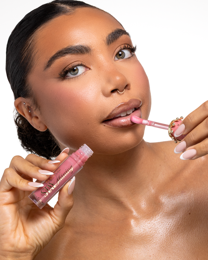Zbliżenie kobiety nakładającej różowy płynny produkt do ust P.Louise Stay Shining Lip Oil z aplikatorem w kształcie łapy łani, trzymając tubkę w drugiej ręcznie, na czystym białym tle.