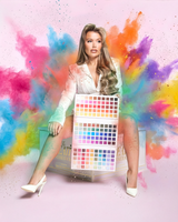 Paige trzyma paletę cieni do powiek P.Louise Creative Comeback XXXL Rainbow z kolorowymi plamami za sobą