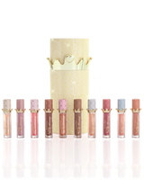 Zestaw dziesięciu produktów P.Louise Christmas Stay Shining Lip Oil ułożonych w rzędzie przed błyszczącym złotym cylindrycznym pudełkiem z olejkiem do ust ze złotą pokrywką, na czystym białym tle.