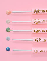 5 brokatowych eyelinerów P.Louise Glisten To Your Heart ułożonych w linię z kropelką produktu na końcu na różowym tle