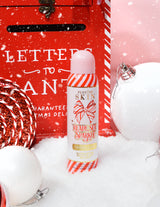 Butelka P. Louise Ready Set Sparkle Christmas Glitter Setting Spray otoczona świątecznymi dekoracjami, takimi jak śnieg, bombki i świąteczna skrzynka na listy